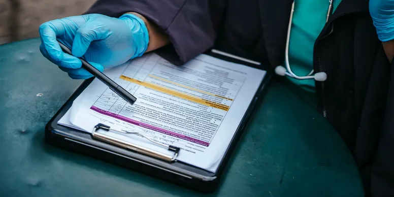 Gloved hand pointing at document on clipboard.